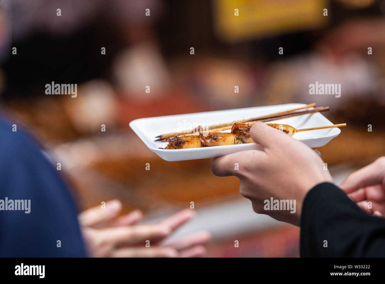 Libre de l'homme hands holding brochette de pétoncles sur brochette stick sur le plateau ou le bac en plein air de la rue du marché Tsukiji à Ginza, Tokyo Japon Banque D'Images