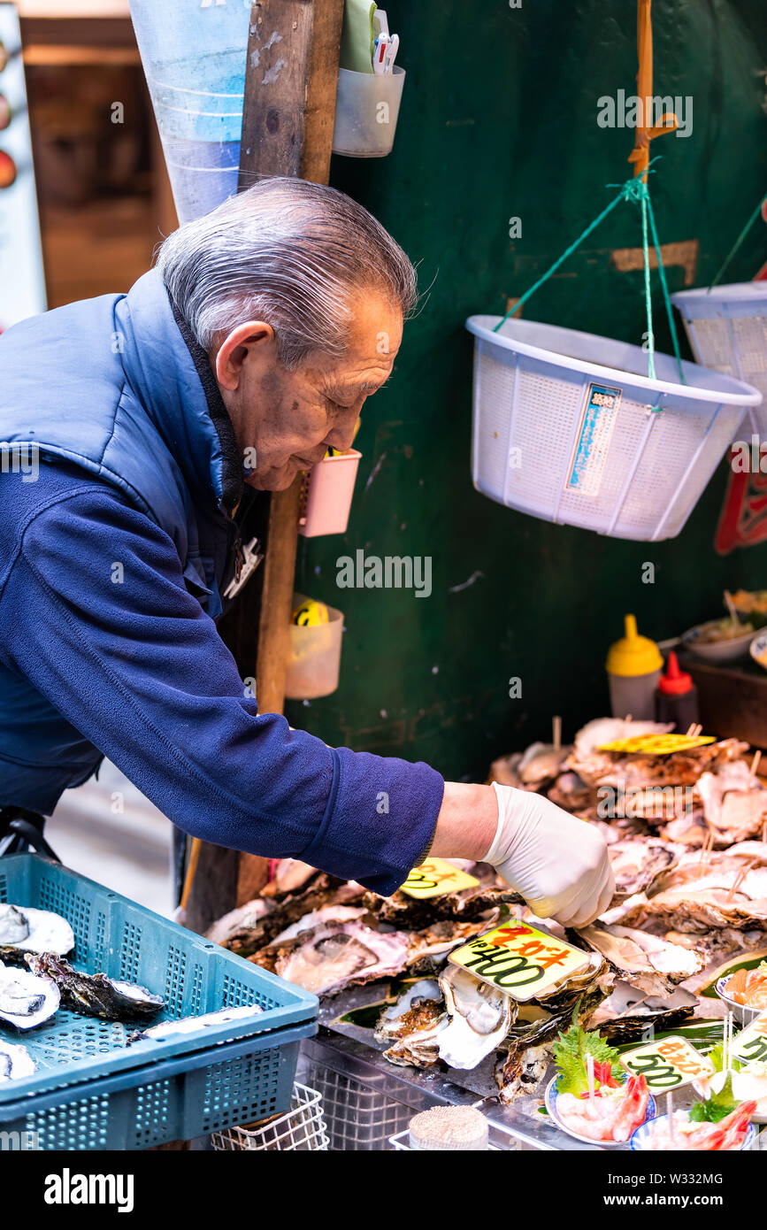 Tokyo, Japon - 30 mars 2019 : vendeur travailleur japonais, l'homme l'organisation mettant les huîtres crues en coque à Ginza marché aux poissons de Tsukiji, rue de la mer Banque D'Images