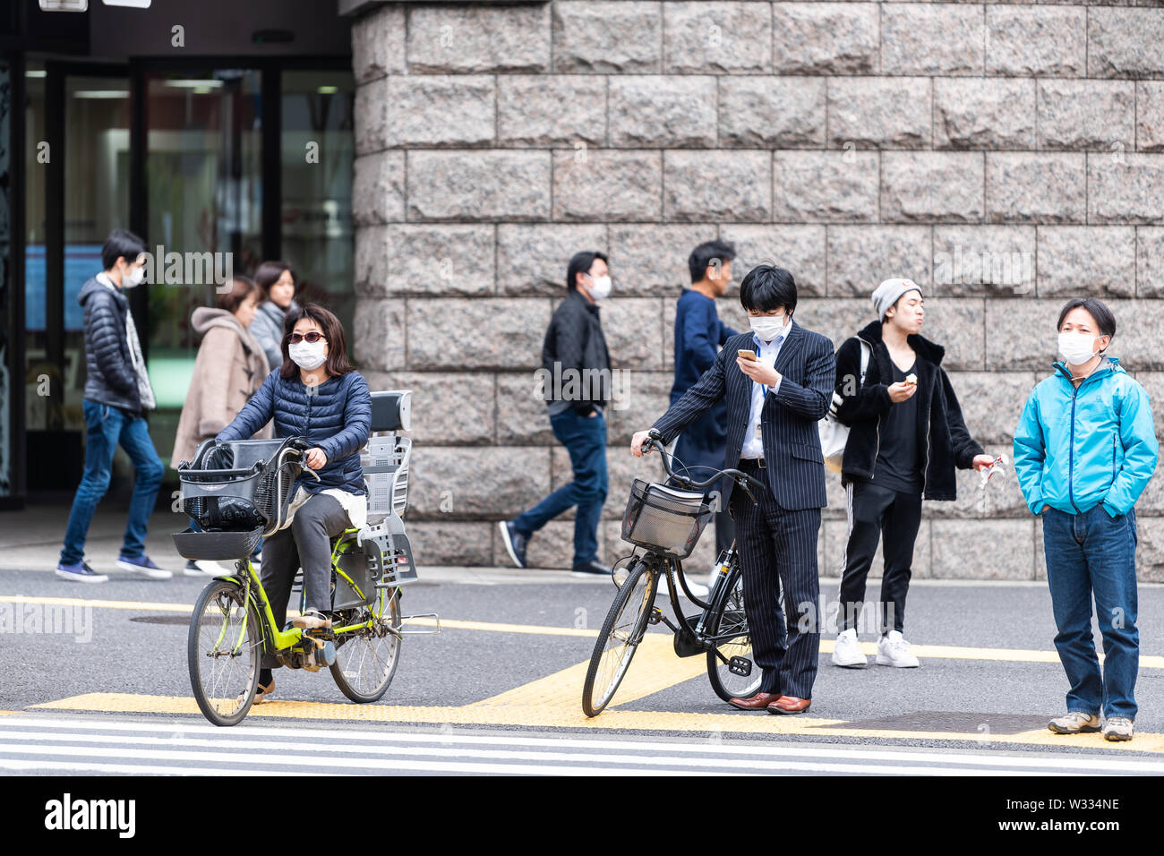 Tokyo, Japon - 1 Avril 2019 : trottoir de la rue de Shinjuku avec des gens qui attendent pour traverser la chaussée routière par bâtiment de station au cours de jour Banque D'Images