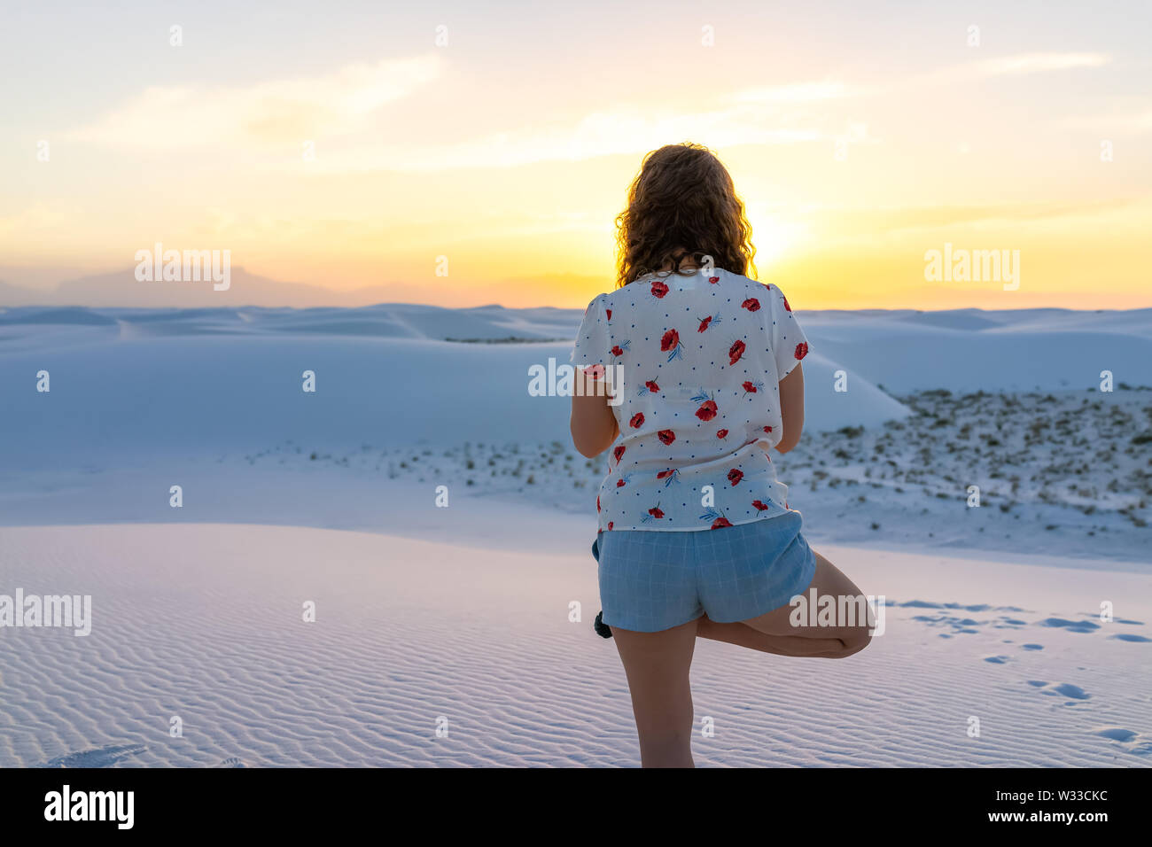 Fille de l'exercice en équilibre sur une jambe à White Sands dunes national monument à Nouveau Mexique vue sur le coucher du soleil Banque D'Images