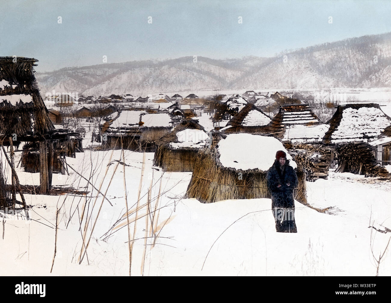 [ 1890 - Japon village ainu, Hokkaido ] - Une femme aïnou se tient dans la neige. Derrière elle un village ainu est visible. 19e siècle vintage lame de verre. Banque D'Images