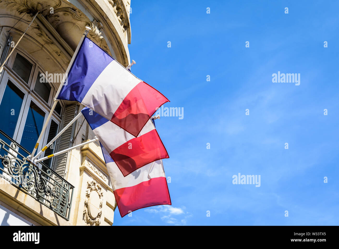 Low angle view of trois drapeaux français de terrasse un immeuble haussmannien à Paris, en France, sur une journée ensoleillée. Banque D'Images
