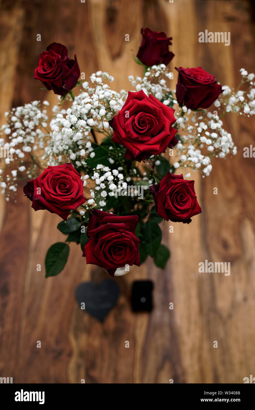 Groupe de sept belles roses rouges avec bague de fiançailles et pierre gravée en forme de coeur debout sur une table en bois Banque D'Images