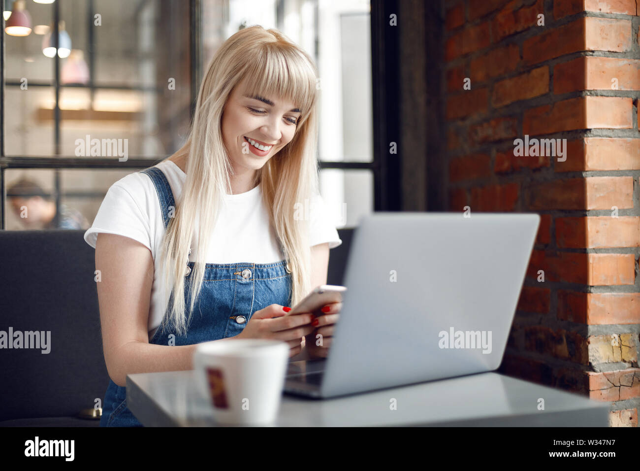 Beautiful woman using mobile phone and laptop while sitting at cafe. Jeune fille au café à boire du café et à l'aide d'achat en ligne pour smartphone Banque D'Images