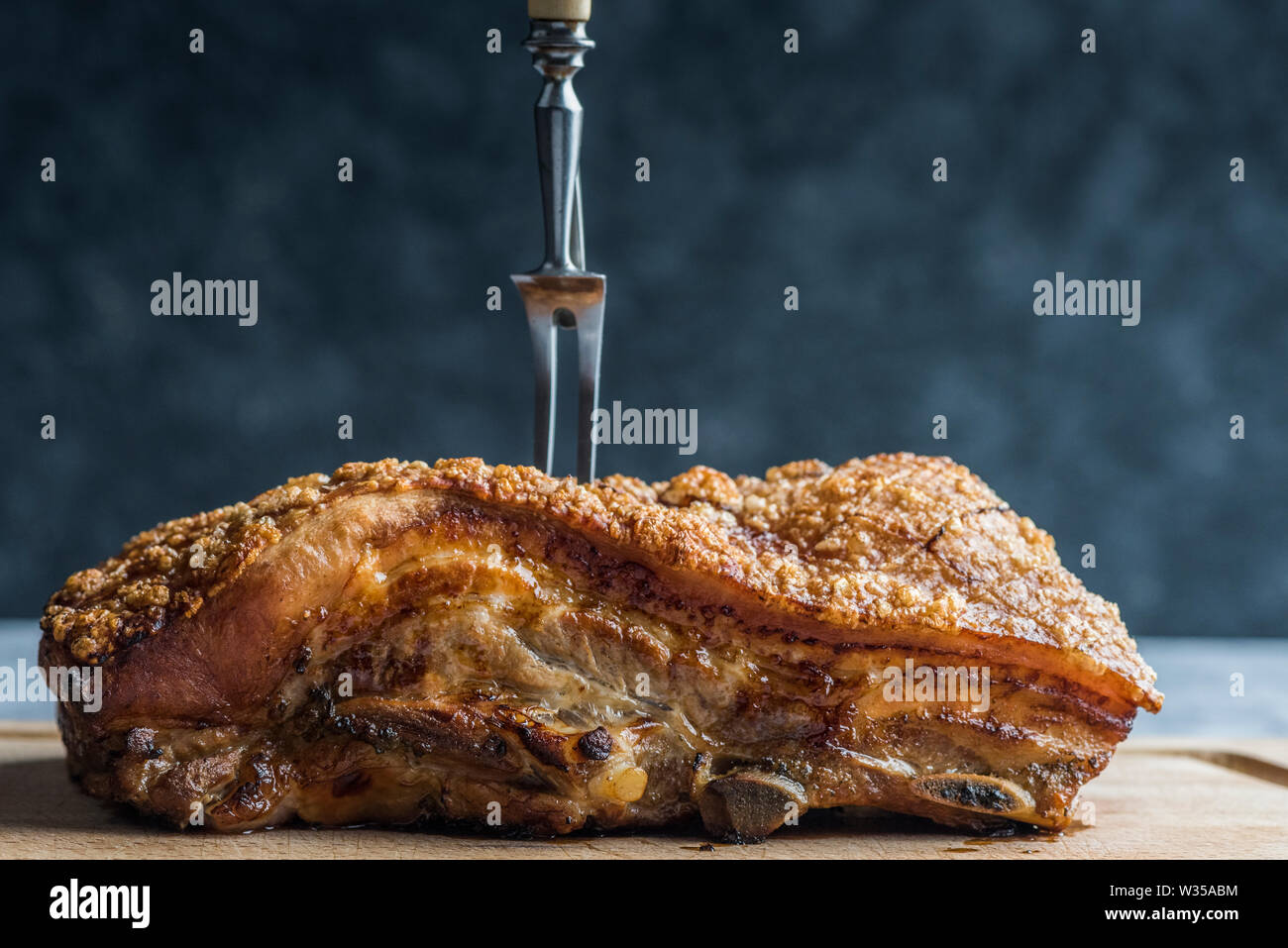 Grand morceau de porc rôti, croustillant de grésillement, empalé avec une fourchette à découper sur une planche en bois Banque D'Images