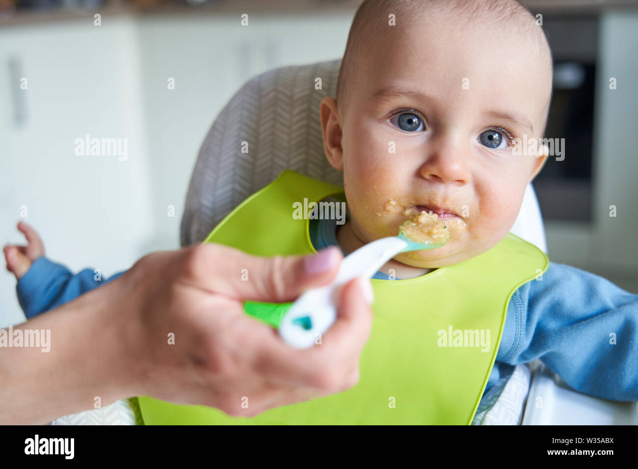 Portrait Of Smiling Baby Boy à la Chaise d'être nourris de la nourriture solide par Mère avec cuillère Banque D'Images