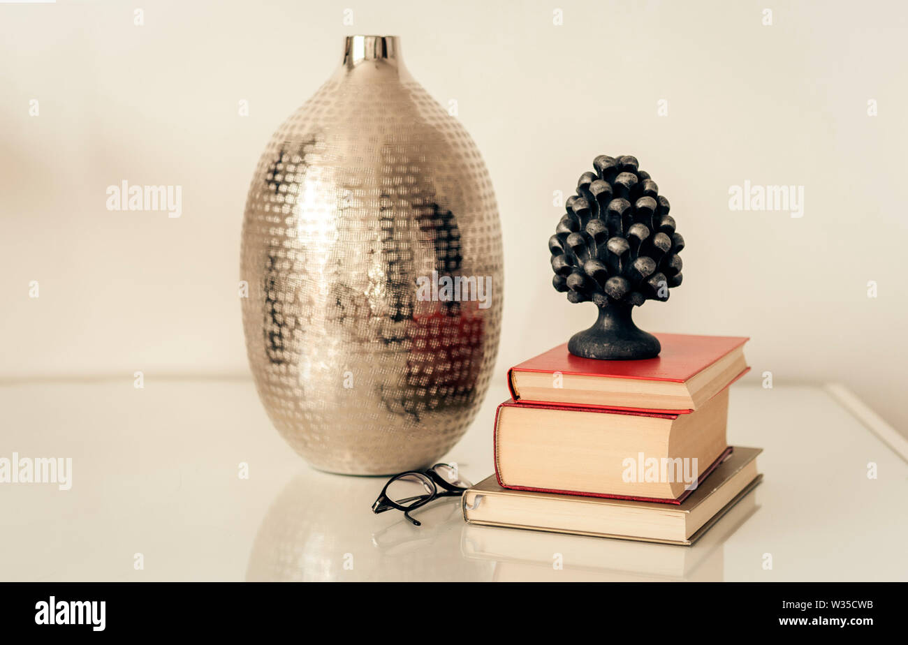 Accueil chaleureux, décoration d'intérieur vase métal, pile de livres, les verres sur une table de chevet en verre blanc Banque D'Images