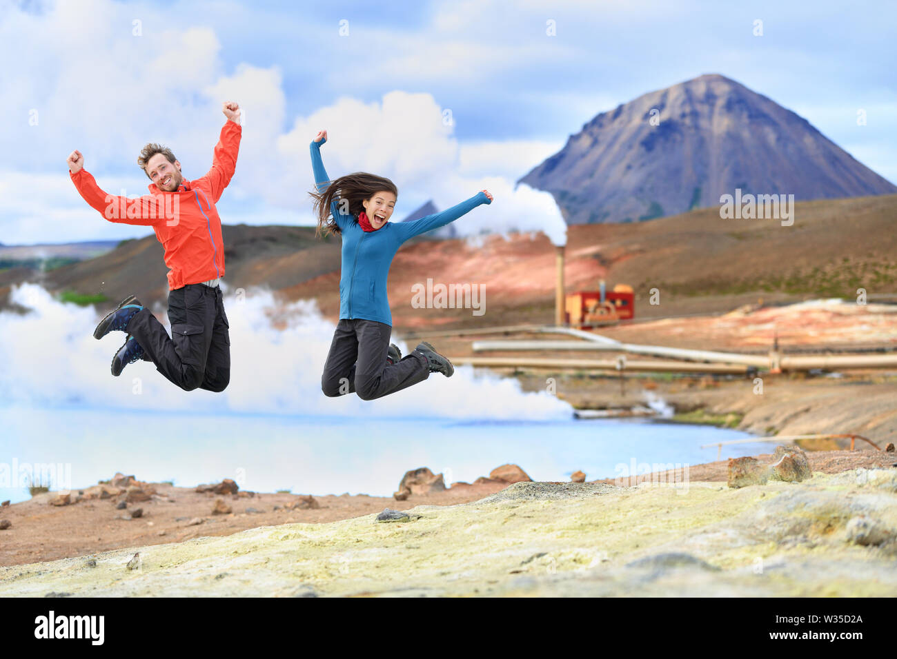 Les gens de voyage Islande sautant de joie en face de Hot Spring et de l'énergie géothermique à Namafjall dans le lac Myvatn. Couple heureux sur les voyages dans la nature islandaise paysage, Route 1 Ring Road. Banque D'Images