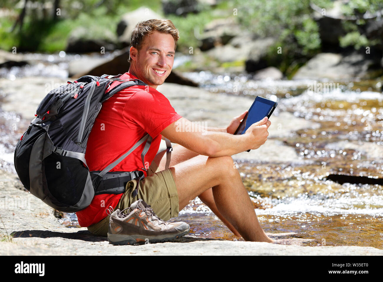 Ordinateur tablette homme hiker relaxing by river holding ebook reader lire livre ou site, randonnées dans le parc Yosemite, USA en utilisant app voyage ou carte pendant la randonnée. Banque D'Images