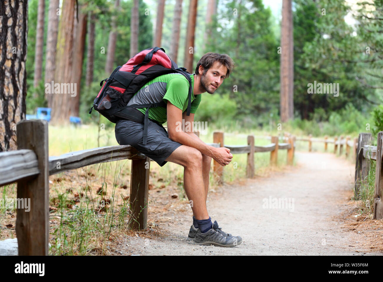 Portrait de l'homme sac à dos de randonnée avec les jambes fatiguées se reposer après une longue randonnée dans la nature. Caucasian man smiling happy avec forêt en arrière-plan lors de voyage d'été dans la région de Yosemite National Park, California, USA. Banque D'Images