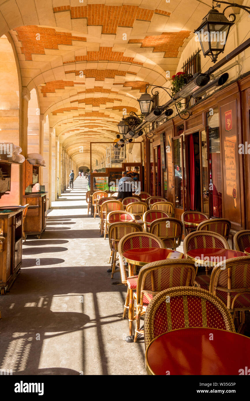 Café terrasse avec tables et chaises, sous les arcades de la Place des Vosges, Paris, France. Banque D'Images