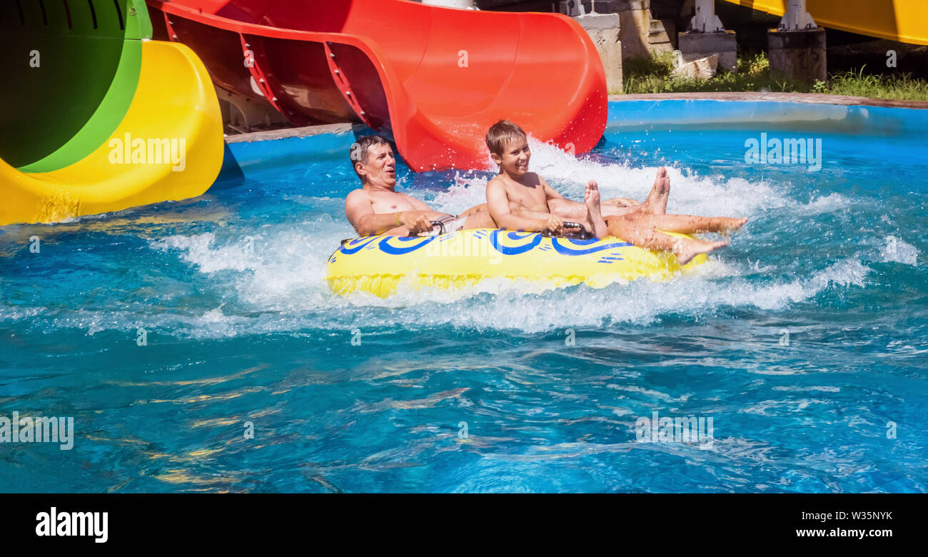 En descendant de la famille juste après le parc de l'eau glisser dans l'anneau gonflable jaune entouré par les projections d'eau. Père et fils sont en week-end d'été Banque D'Images