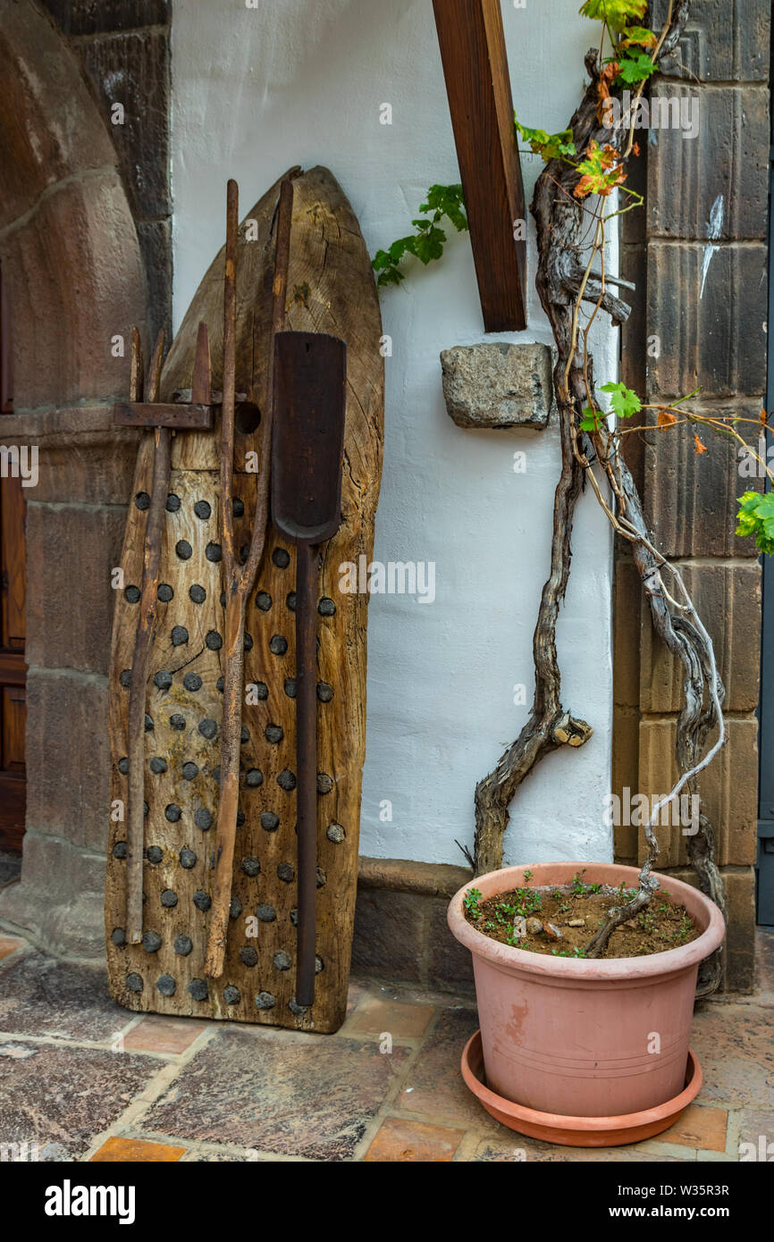 Vintage ancienne batteuse traditionnelle faite de bois et de silex avec d'autres instruments d'agriculture s'appuya contre le mur et une vieille vigne longue et énorme Banque D'Images