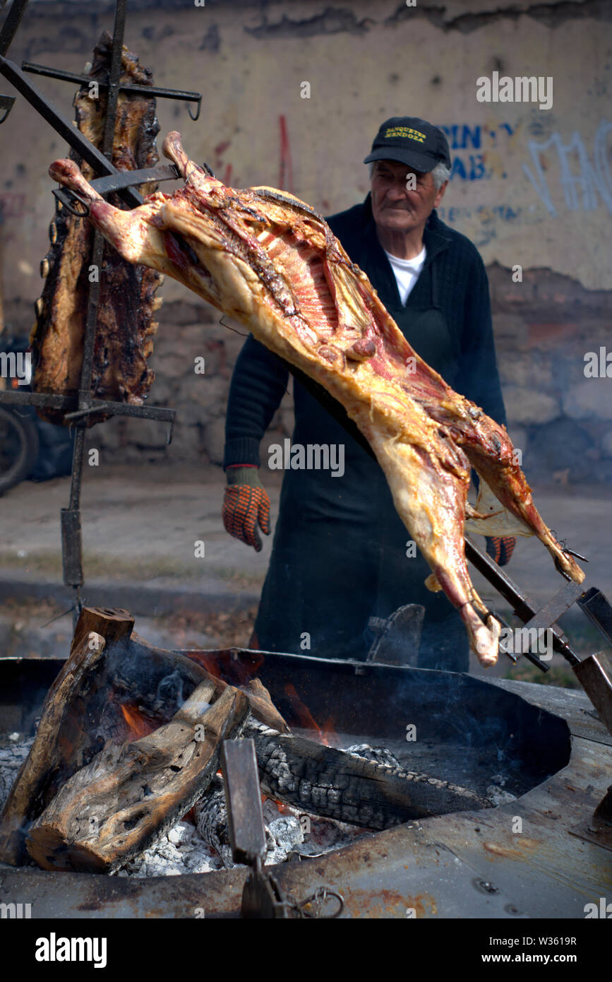 Un vieil homme la cuisson une chèvre sur les flammes, sur un barbecue argentin typique. Banque D'Images