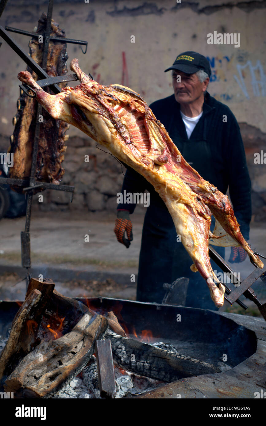 Un vieil homme la cuisson une chèvre sur les flammes, sur un barbecue argentin typique. Banque D'Images
