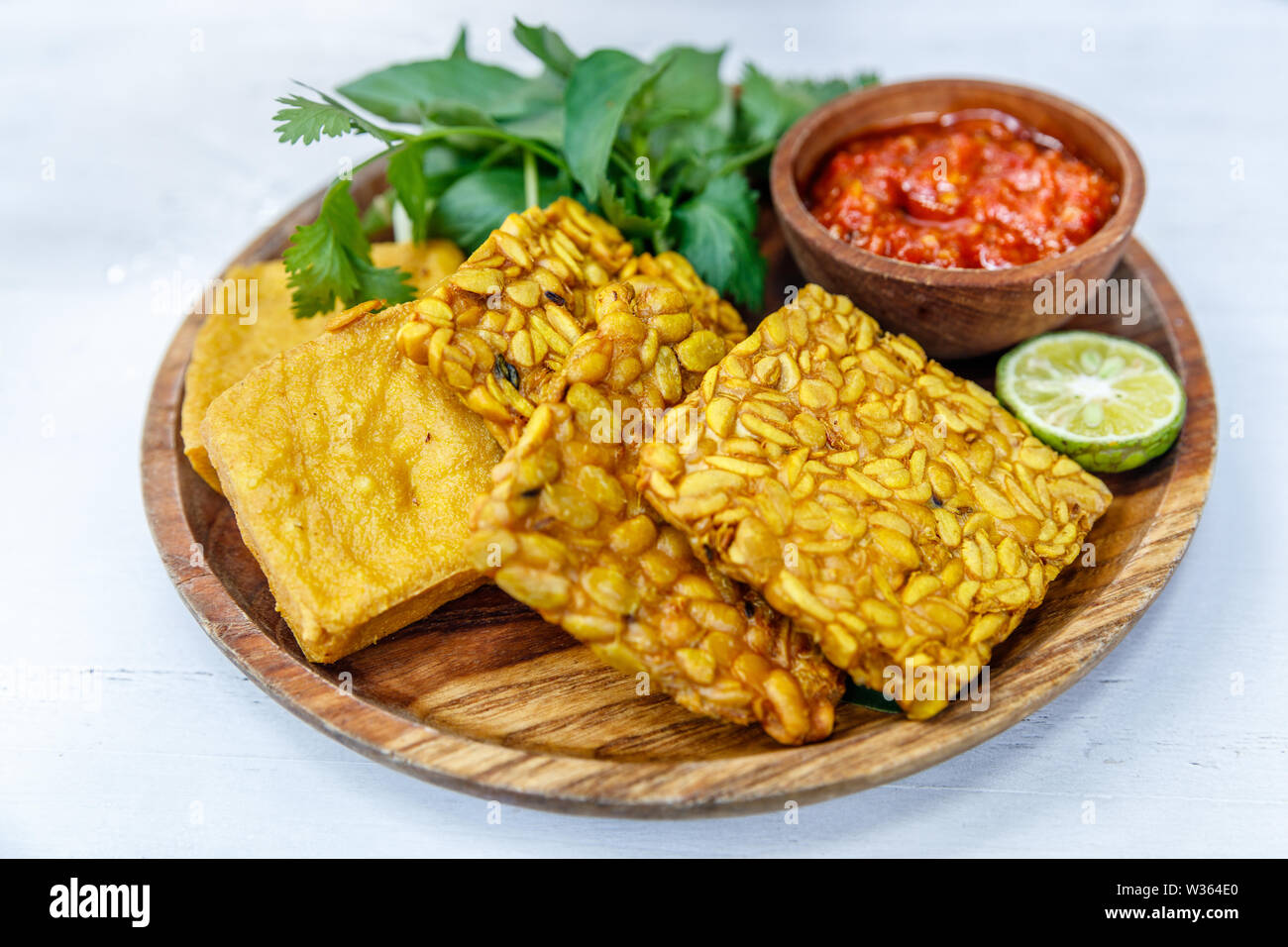 Le tempeh et le tofu frit servi avec sauce sambal épicé et de la chaux. Sur une plaque en bois rond. Vue de côté Banque D'Images