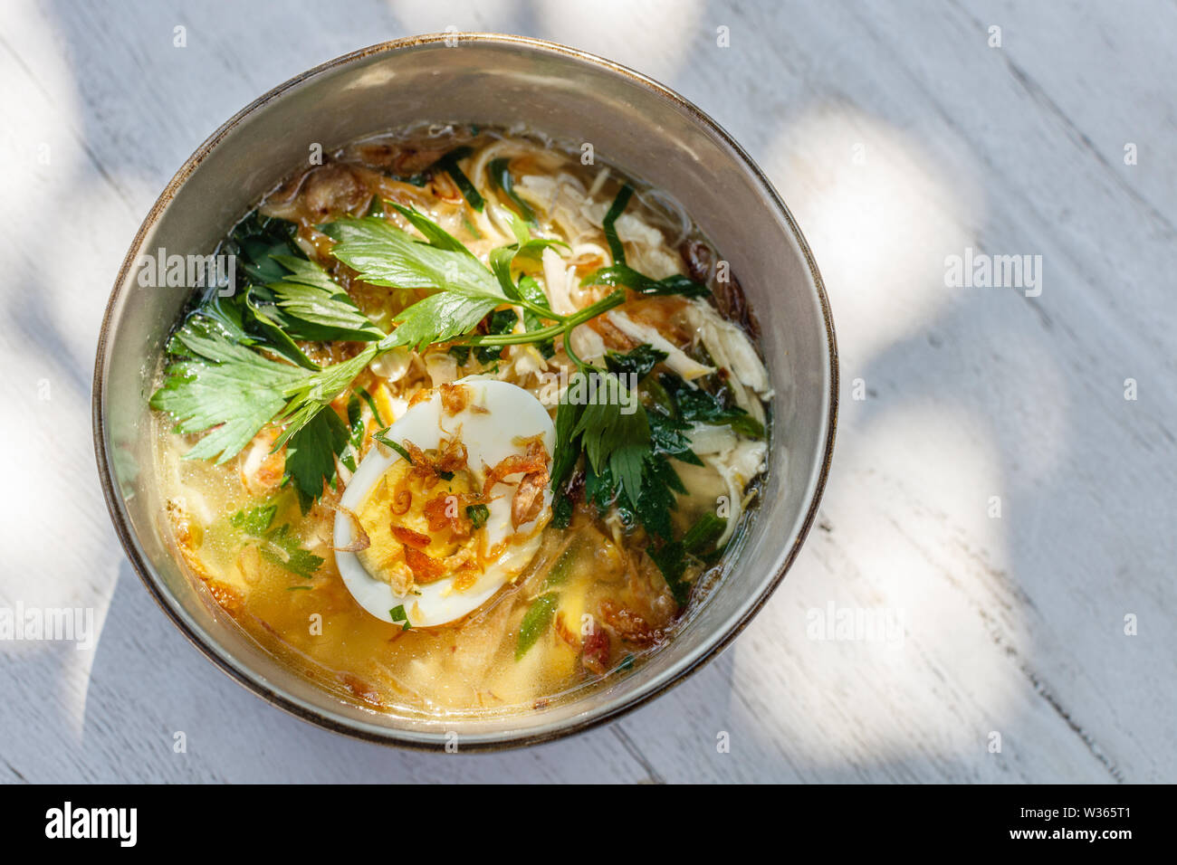 Soto ayam, une soupe de poulet jaune avec oeuf dur, persil et bawang goreng (oignon frit). Une cuisine indonésienne. Banque D'Images