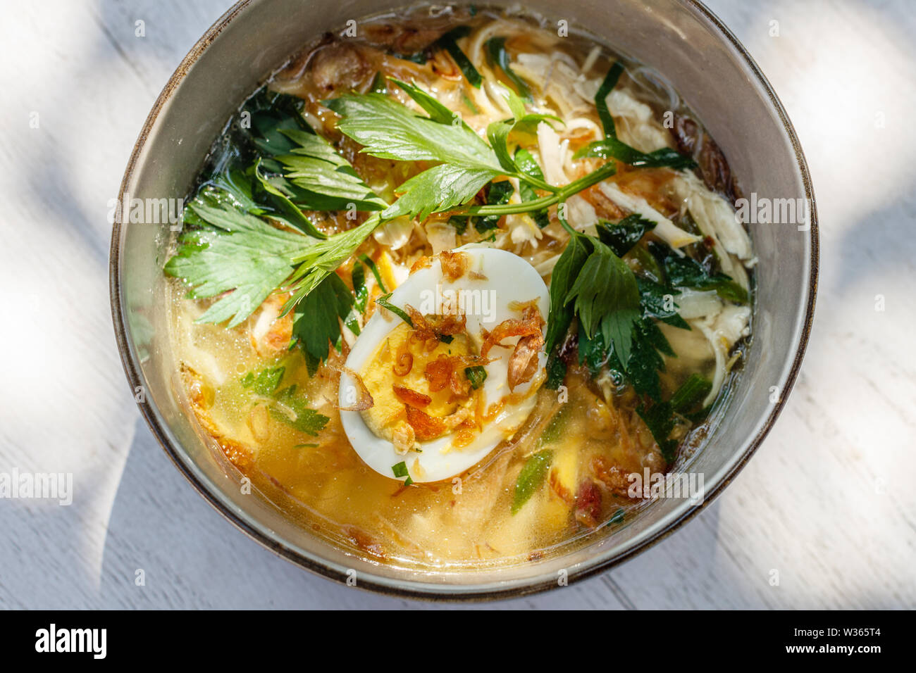 Soto ayam, une soupe de poulet jaune avec oeuf dur, persil et bawang goreng (oignon frit). Une cuisine indonésienne. Banque D'Images