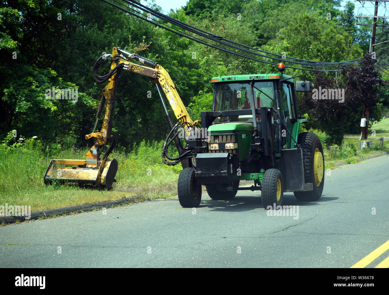 Tracteur avec un accessoire tondeuse hydraulique de la tonte de l'herbe en bordure de la route. Banque D'Images