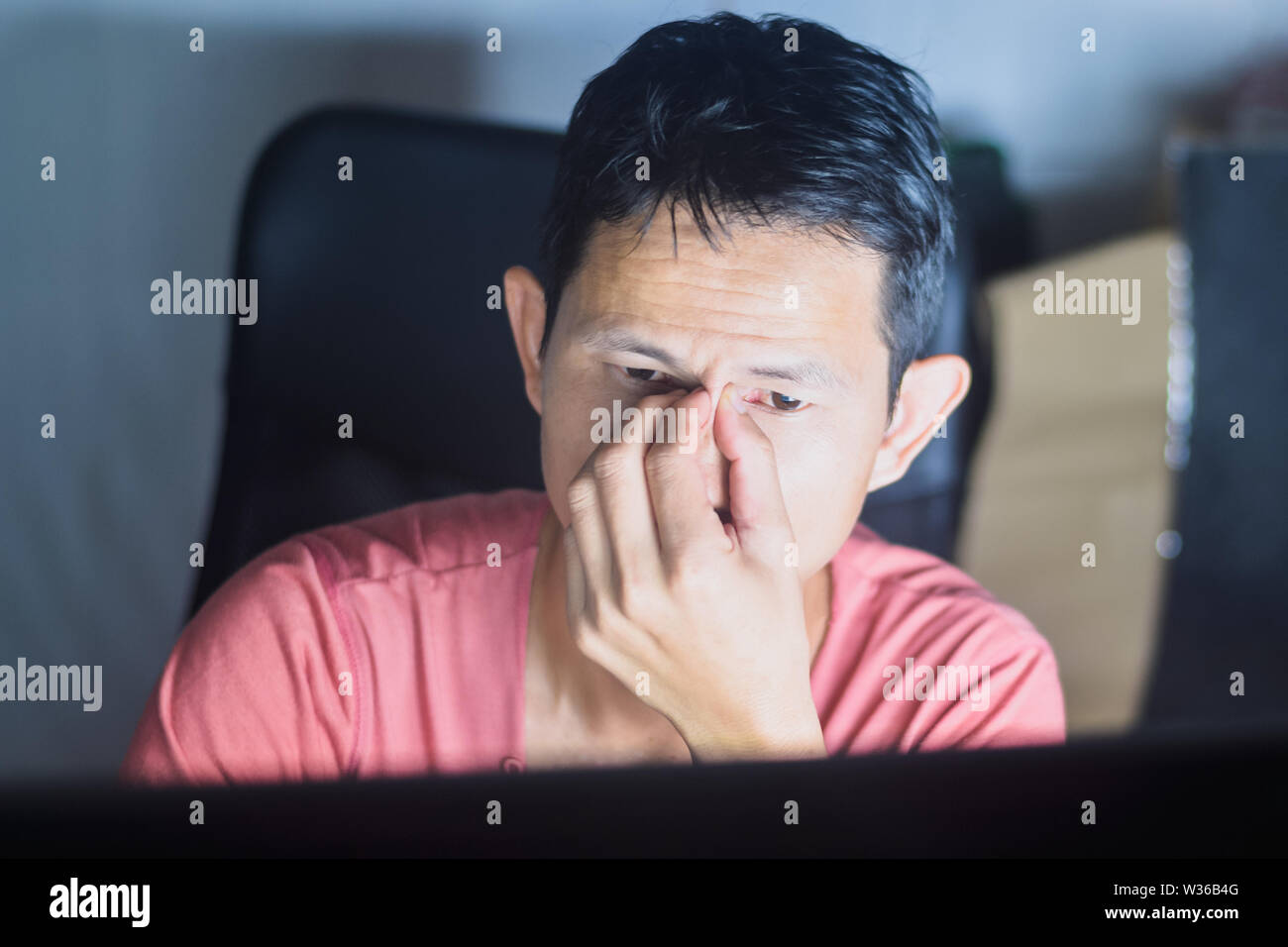 Un homme ayant la fatigue Maux de tête au bureau à l'ordinateur tout en regardant totalement épuisé travailler tard dans la nuit. Banque D'Images
