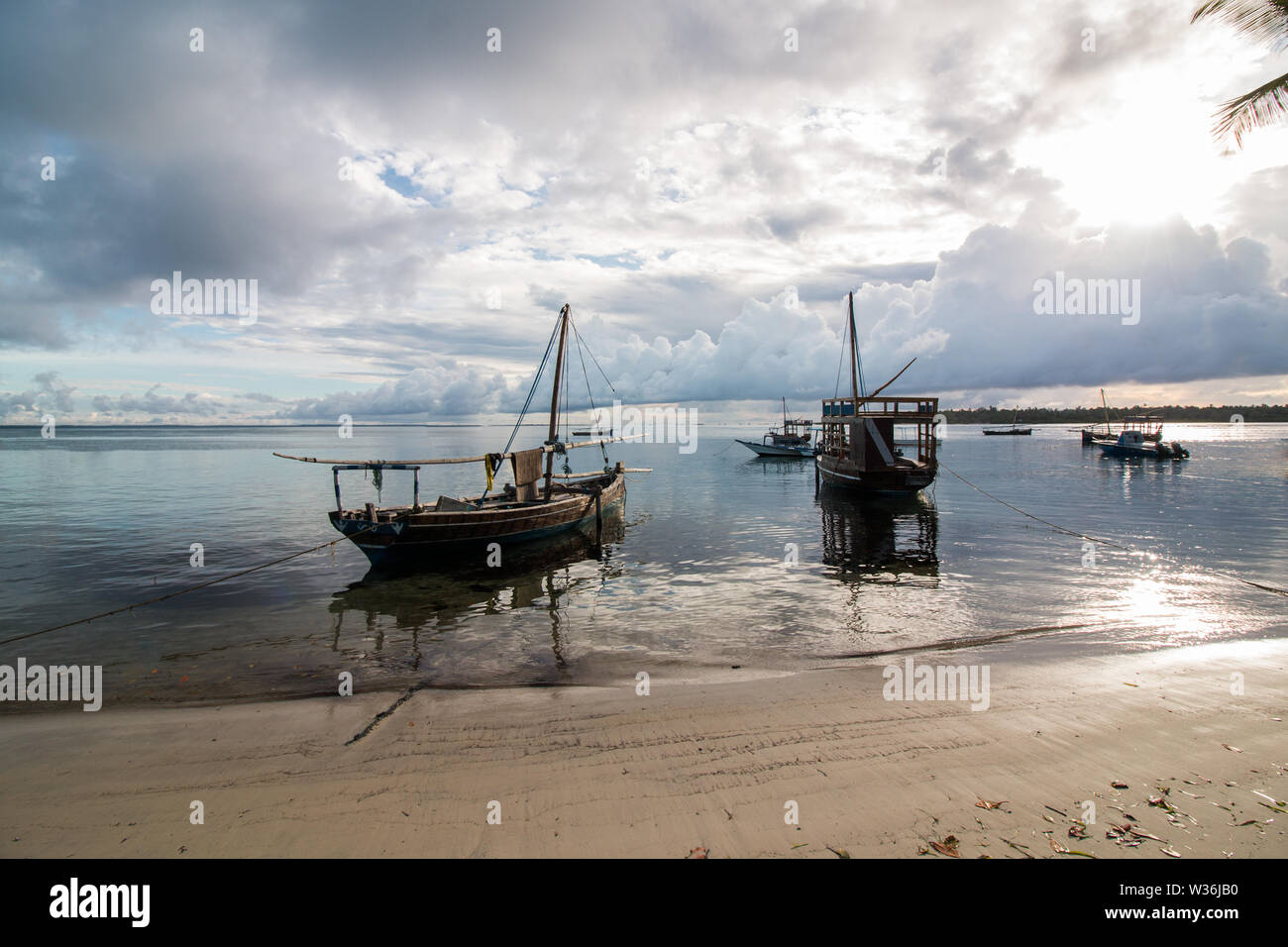 Les petits voiliers en bois, sur l'eau à la plage au lever du soleil à l'île de Mafia, la Tanzanie, avec ciel nuageux et calme avec de l'eau entourant les pirogues. Banque D'Images