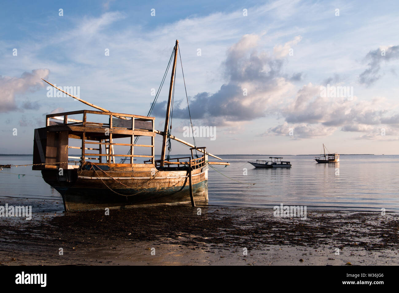 Un grand voilier en bois, sur l'eau à la plage au lever du soleil à l'île de Mafia, la Tanzanie, avec ciel nuageux et calme de l'eau. Banque D'Images