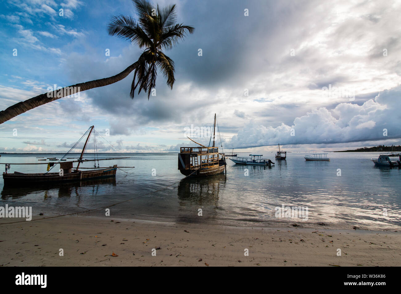 Les petits voiliers en bois, sur l'eau à la plage au lever du soleil à l'île de Mafia, la Tanzanie, avec ciel nuageux et calme avec de l'eau entourant les pirogues. Banque D'Images
