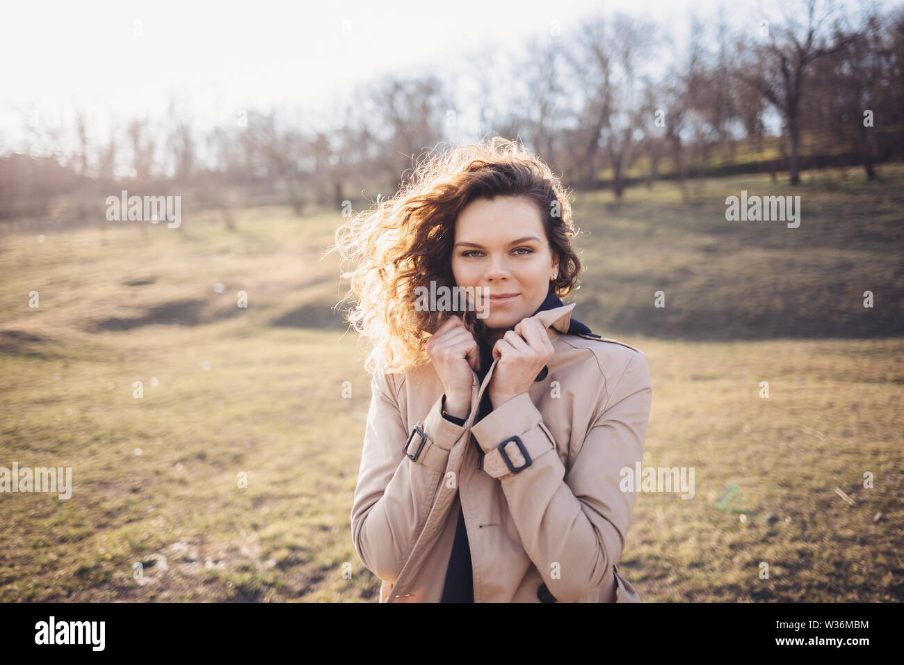 Portrait de jeune femme portant un élégant manteau beige col tenant contre le vent. Female standing outdoors in sunlit champ sur une journée d'automne. Banque D'Images