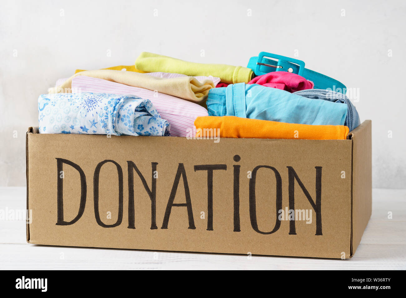 Donation box avec différents vêtements colorés sur une table. Banque D'Images