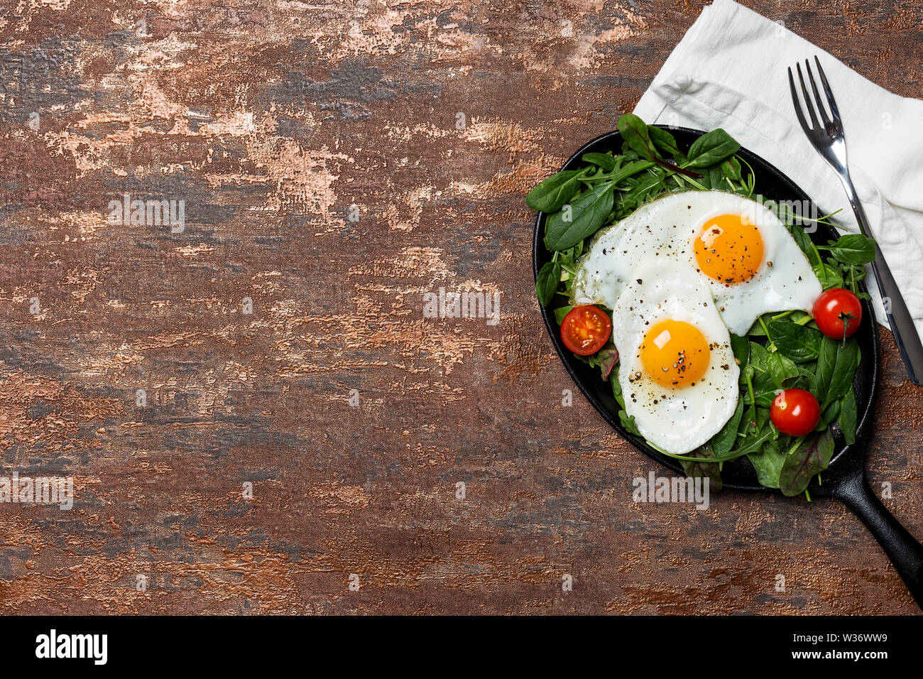 Pan avec les œufs et les tomates cerises et les salades vertes à fond brun. Serviette et près de la fourche. Concept d'alimentation saine. Mise à plat, vue du dessus, copiez Banque D'Images Pan avec les œufs et les tomates cerises et les salades vertes à fond brun. Serviette et près de la fourche. Concept d'alimentation saine. Mise à plat, vue du dessus, copiez Banque D'Images