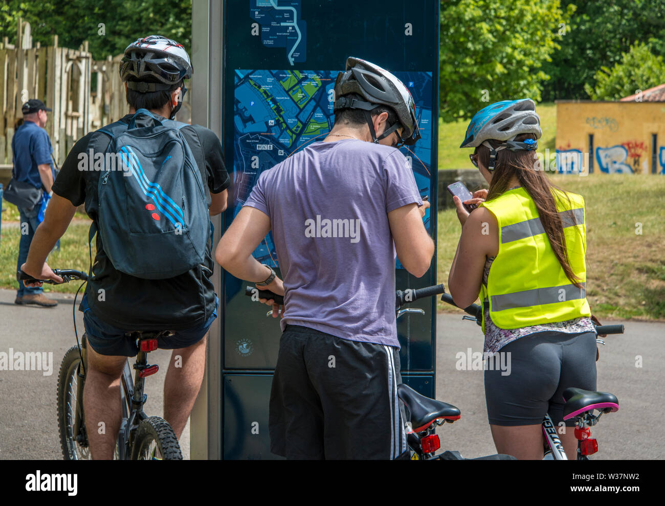 Deux hommes et une femme les cyclistes d'arrêter de naviguer en utilisant la piste cyclable plan guide de la ville et leurs téléphones cellulaires à proximité de parc du château. Bristol, Royaume-Uni Banque D'Images