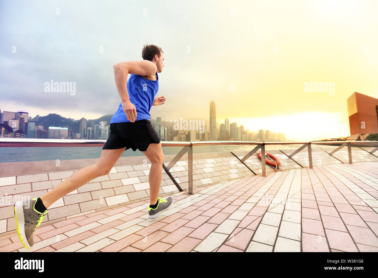 Urban running man runner à Hong Kong sur la ville. Portrait homme travaillant sur le jogging sur la promenade du port de Victoria de Hong Kong, Chine, en après-midi, coucher du soleil au printemps. Banque D'Images