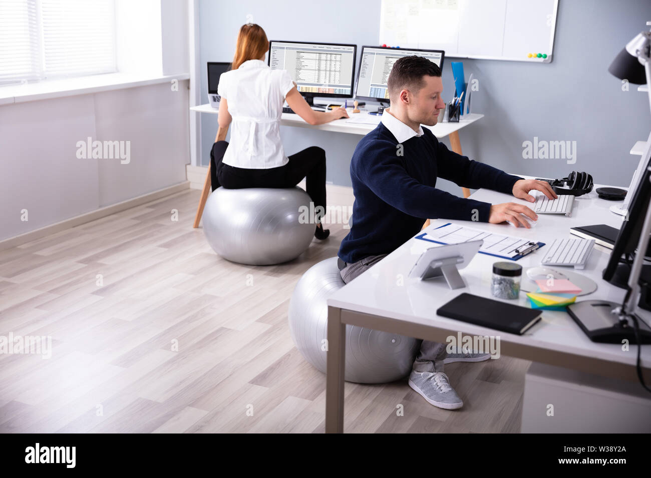 Two Businesspeople working on Computer in Office Sitting on Fitness Ball Banque D'Images