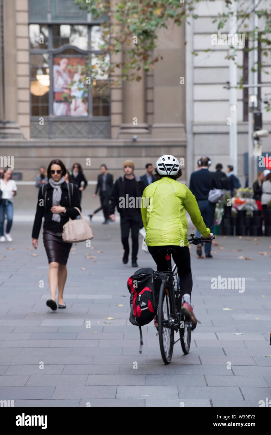 Une femme portant un casque et un imperméable jaune rides son vélo avec une sacoche latérale par Sydney Martin Place sur un matin de la semaine Banque D'Images