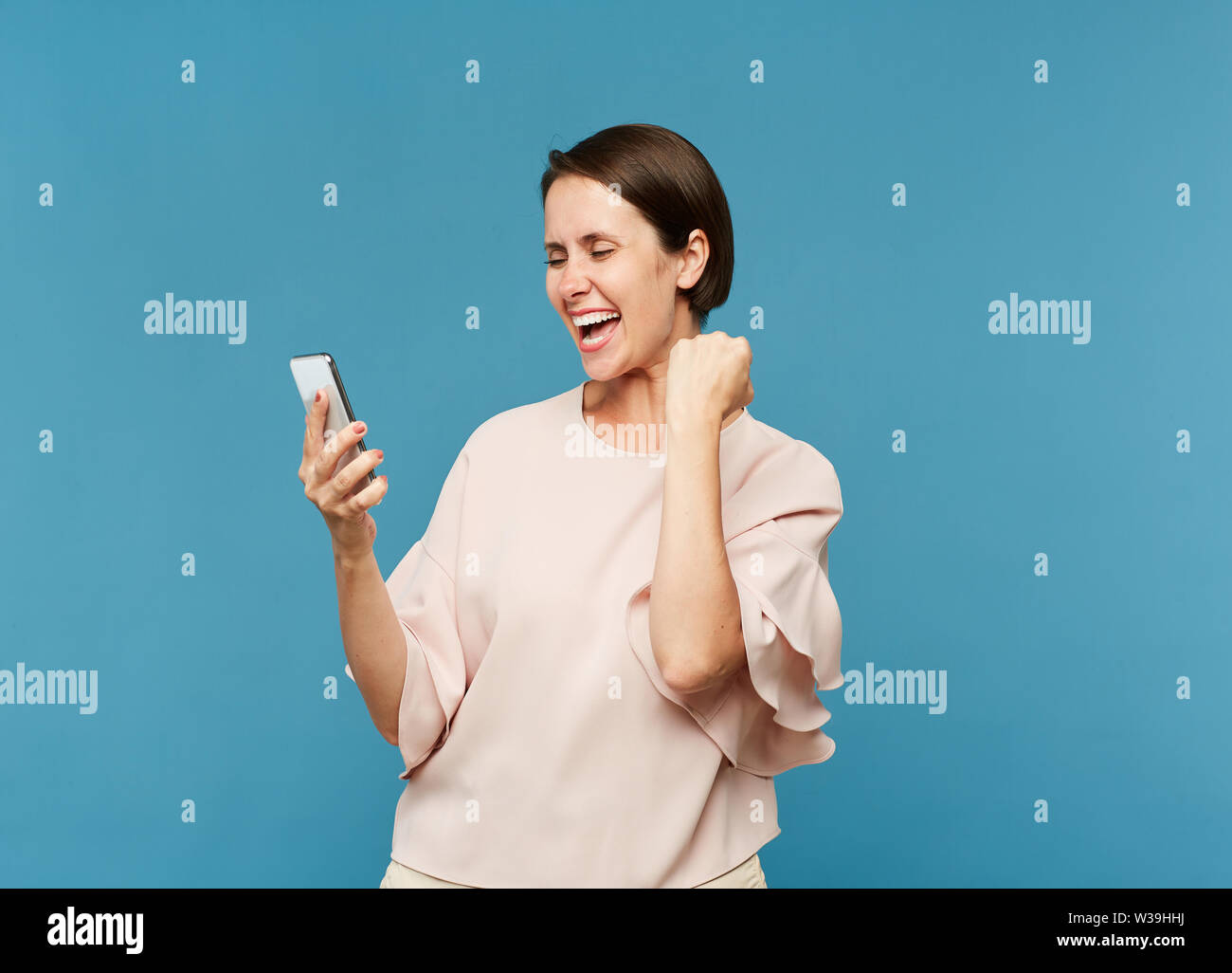 Les jeunes femmes extatiques à la recherche à l'écran du smartphone tout en exprimant la joie dans l'isolement Banque D'Images