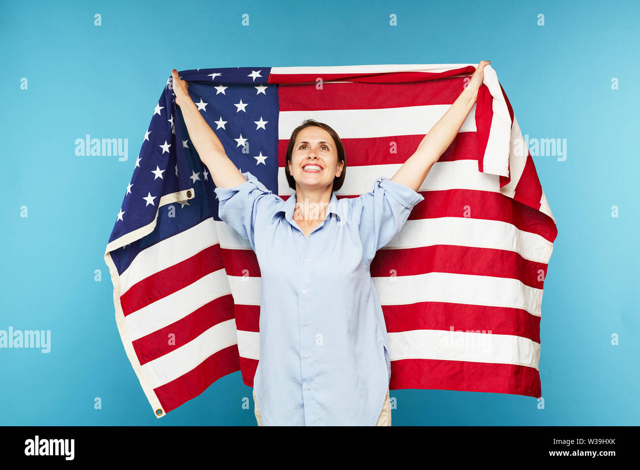 Happy young casual woman raising hand tout en maintenant un grand drapeau américain sur fond bleu Banque D'Images