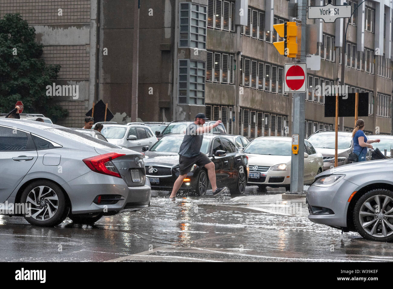 Toronto, Canada. 13 juillet, 2019. Les après-midi la pluie a laissé de nombreuses intersections du centre-ville de Toronto inondées. Sur la photo de la voie par l'eau tandis que les piétons au croisement à New York et de Harbour Street. Credit : EXImages/Alamy Live News Banque D'Images
