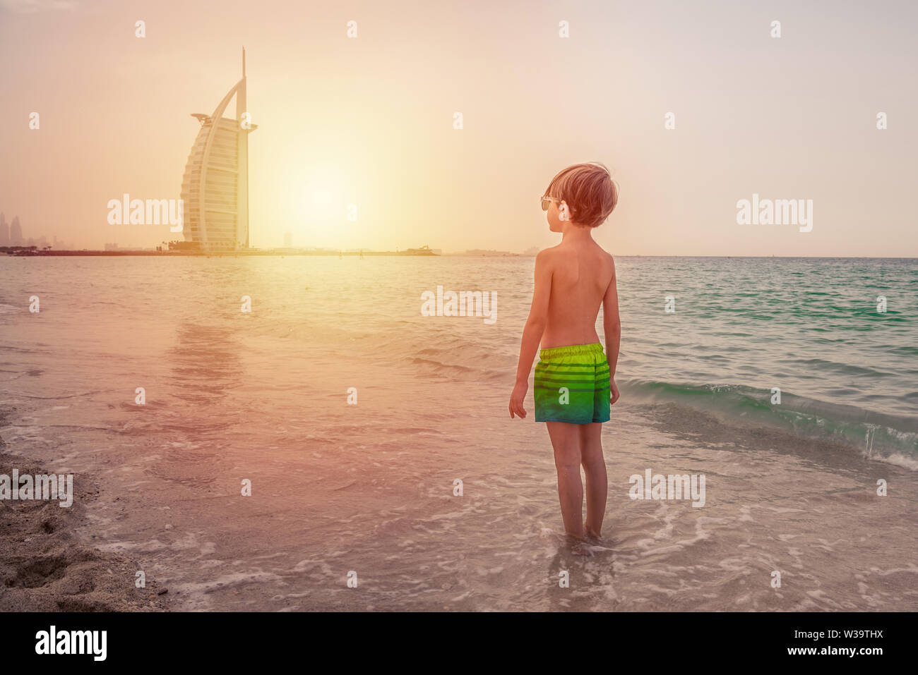 Avec ses pieds dans l'eau, à la mer, à la plage, fasciné par l'incroyable et l'immense bâtiment qu'il voit. Comment l'homme est petite par rapport à ces skysc Banque D'Images