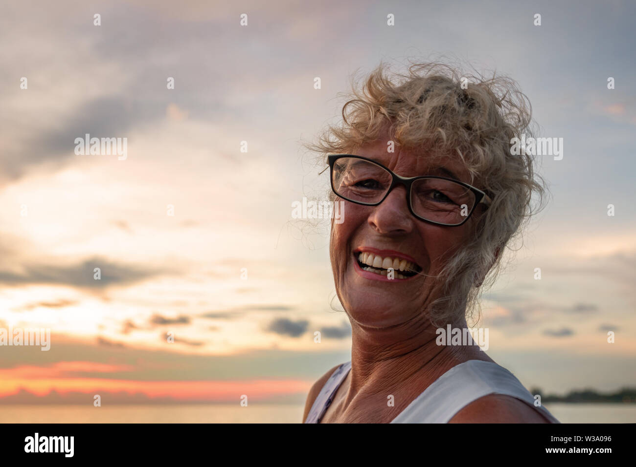 Une vieille femme sourit heureux tannées au coucher du soleil par la mer sur la plage. plein air, soirée, close-up. Banque D'Images