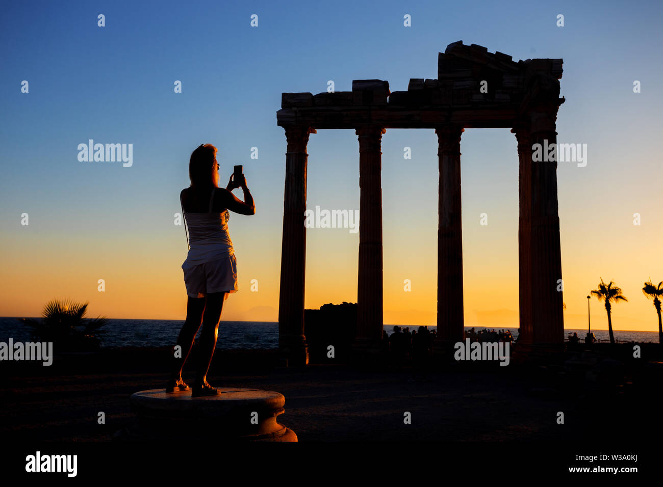 Silhouette d'une fille photographiant au téléphone le Temple d'Apollon au coucher du soleil. Side, Turquie Banque D'Images
