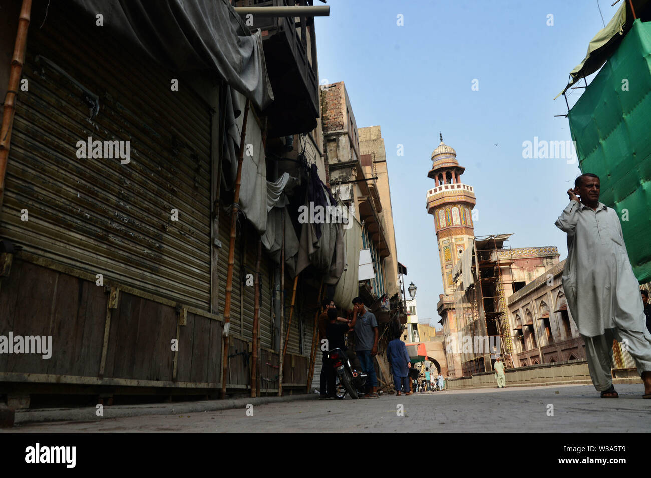 Lahore, Pakistan. Le 13 juillet, 2019. Sur leur chemin au cours de Pakistanais et les hommes d'observer une grève des commerçants d'obturation plus proche Mosquée historique Wazir Khan, Wall city authority sur l'appel de Markaz-e-Tanzeem Tajiran-e- le Pakistan contre sur la mise en œuvre de 17  % Taxe sur la valeur ajoutée pour les traders à Lahore le 13 juillet 2019. Commerçants pakistanais ont en grande partie conservé leur arrêt d'affaires à travers le pays contre le nouveau régime de taxe de vente dans le premier budget du nouveau gouvernement et les partis de l'opposition a dit qu'ils sont venus sur le diktat du Fonds Monétaire International à son tour d'un plan de sauvetage de 6 milliards de dollars. Credit : PACI Banque D'Images