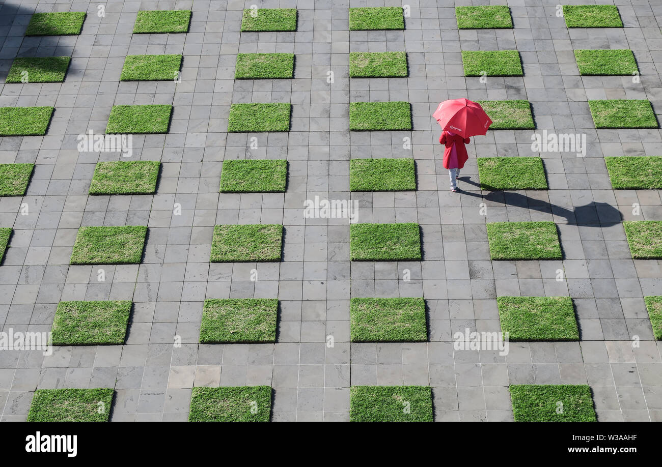 Melbourne, Australie : Rouge parapluie femme marchant à travers la pelouse verte vérifie à Melbourne's Jardins de domaine Banque D'Images