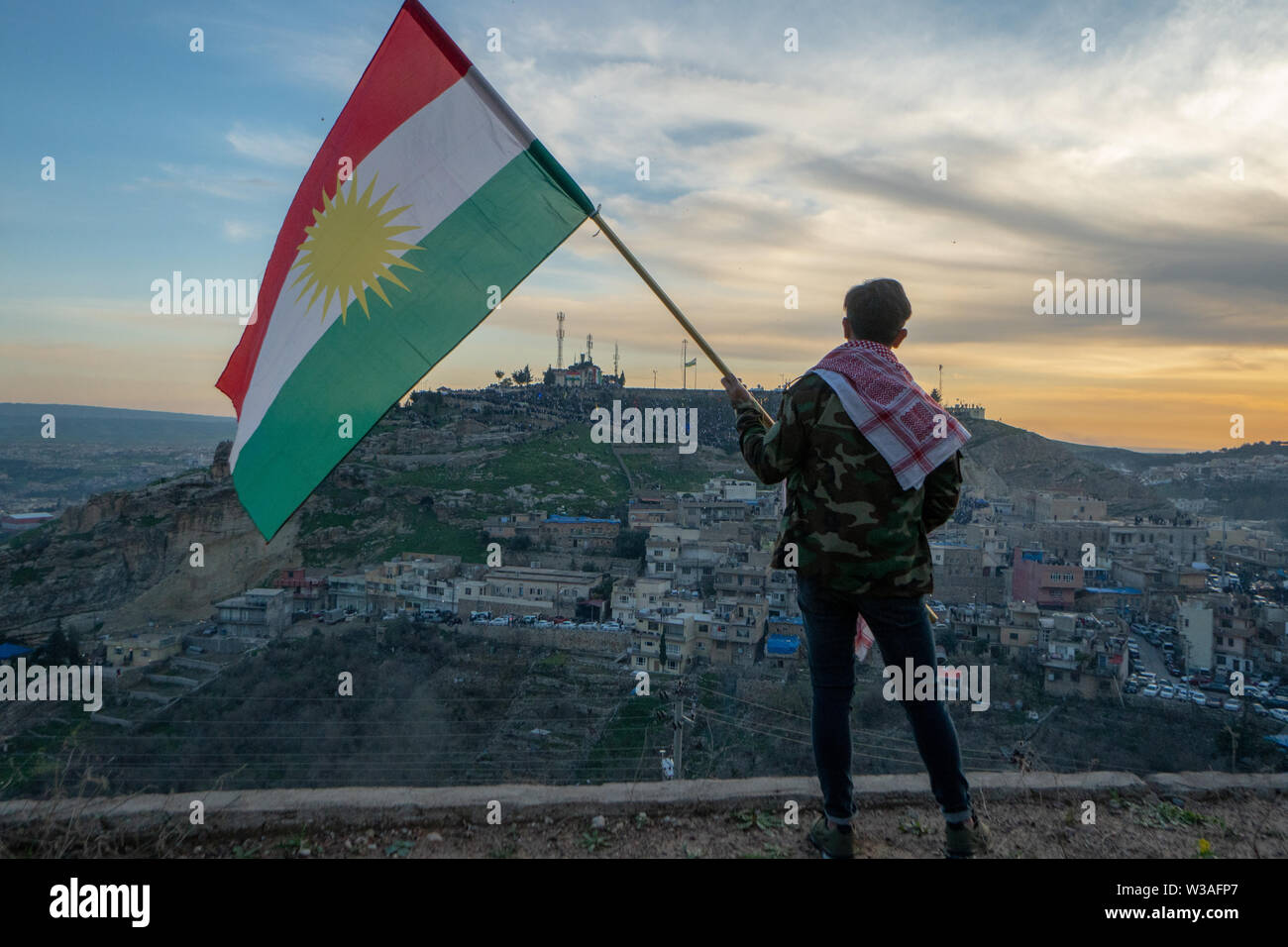 Adolescent tenant le drapeau du Kurdistan dans le nord de l'Iraq à l'heure du coucher du soleil sur le Norouz 2019 Banque D'Images