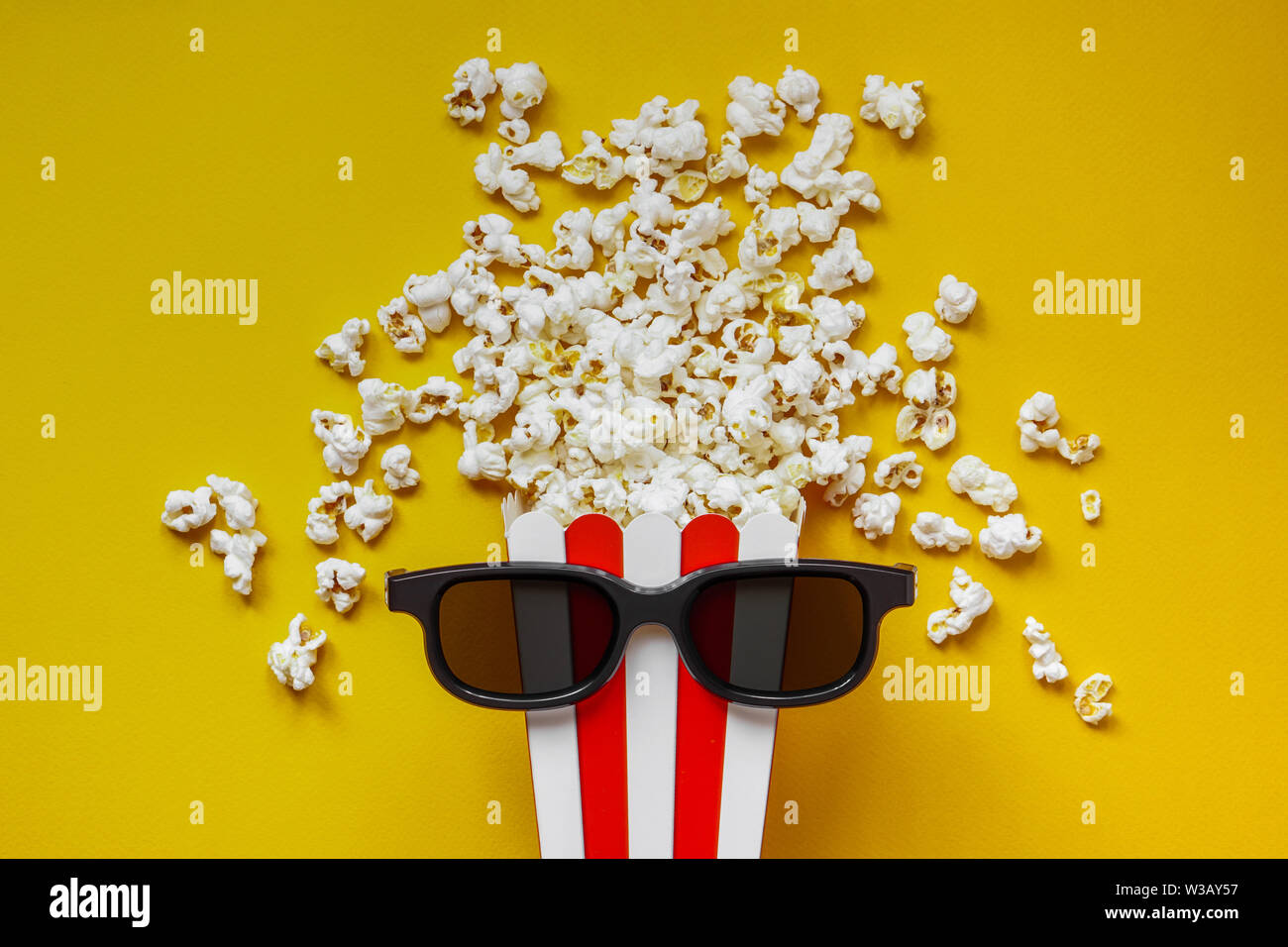 Popcorn dans une boîte en carton rouge et blanc avec des verres pour un film  en 3D sur le dos jaune. Maïs soufflé au godet à rayures rouges sur fond  jaune. Mise