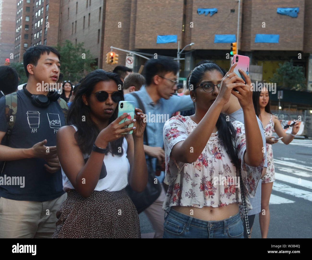 New York, USA. Le 13 juillet, 2019. Les gens prennent des photos au cours d'Manhattanhenge tandis qu'un blackout englouti le côté ouest de Paris . Manhattanhenge, quand le soleil s'aligne parfaitement avec la ville street grille, et ne se produit que quelques fois par année. La panne a perturbé le Westside à partir de la 32e rue à 71st Street de Broadway à l'Ouest l'autoroute. Credit : Nancy/Kaszerman ZUMA Wire/Alamy Live News Banque D'Images