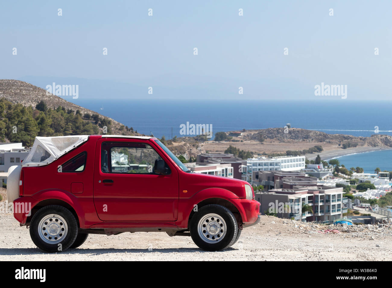 Véhicule tout terrain rouge compacte sur colline, avec vue panoramique et vue sur la mer en arrière-plan. L'île de Kos, Grèce, sur une chaude journée d'été. Banque D'Images
