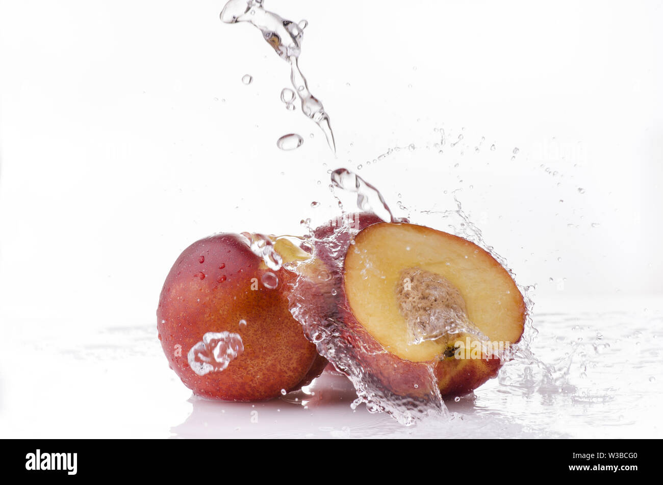Une vague d'eau claire tombe sur certaines pêches nectarines sur un fond blanc Banque D'Images