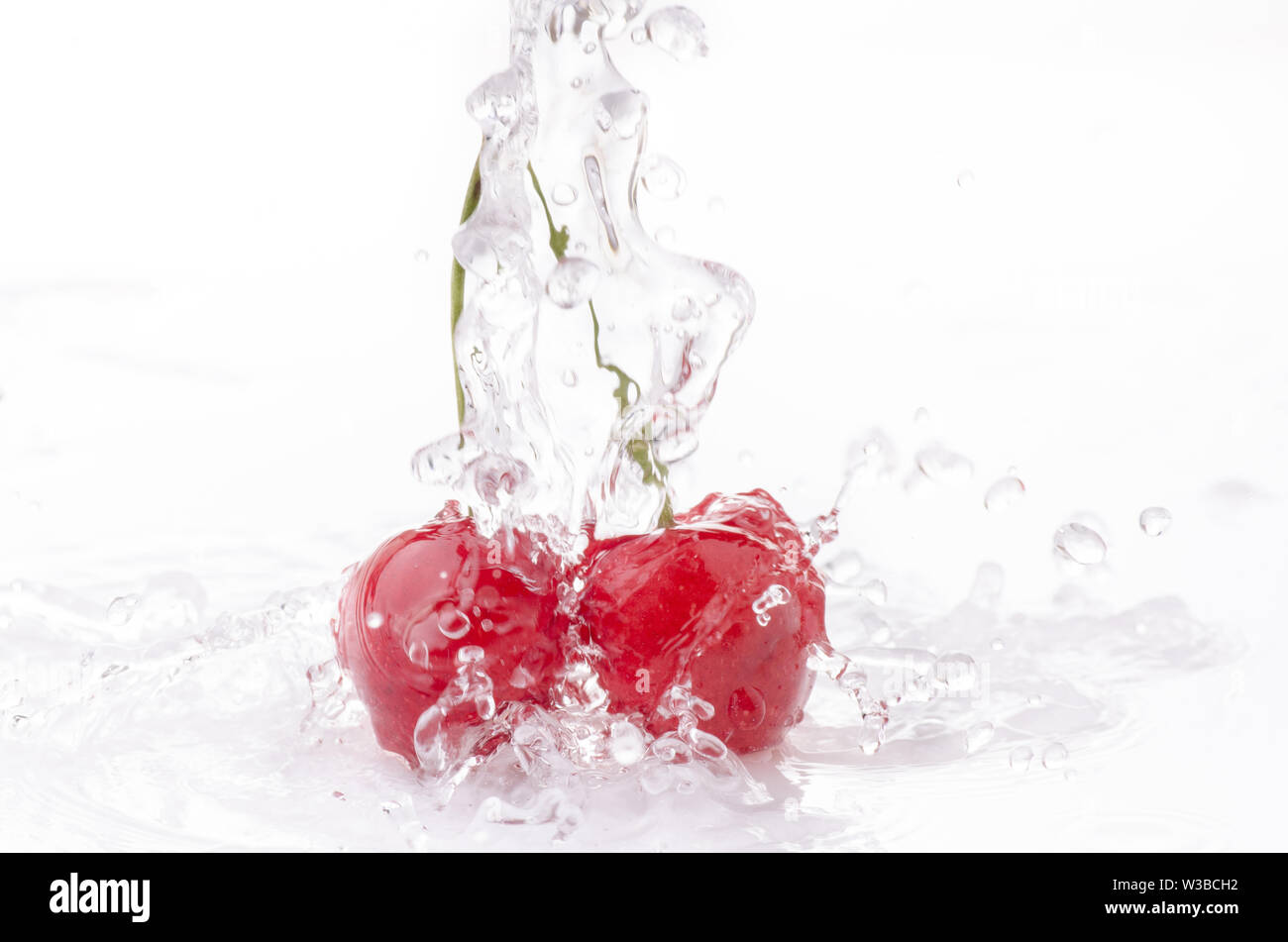 Une vague d'eau claire tombe sur les cerises sur fond blanc Banque D'Images