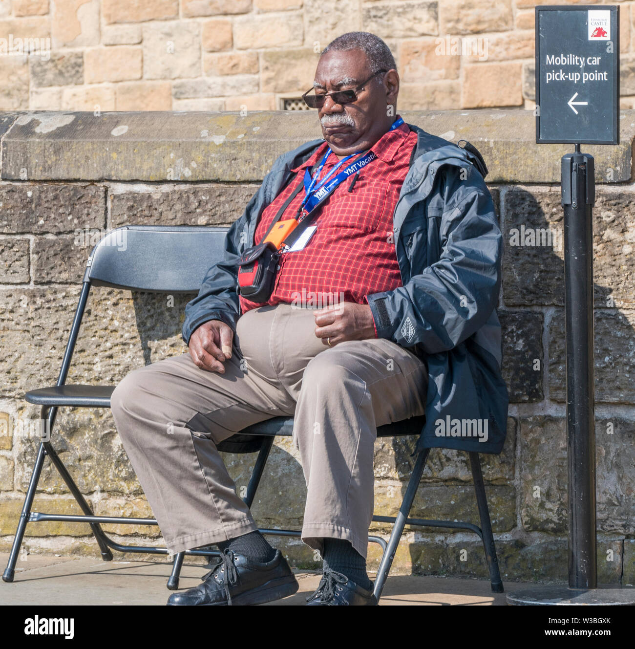 Un vieil homme noir, assis sur une chaise, sommeillant sous le chaud soleil du printemps sur le château d'Édimbourg, promenade. L'Écosse, au Royaume-Uni. Banque D'Images