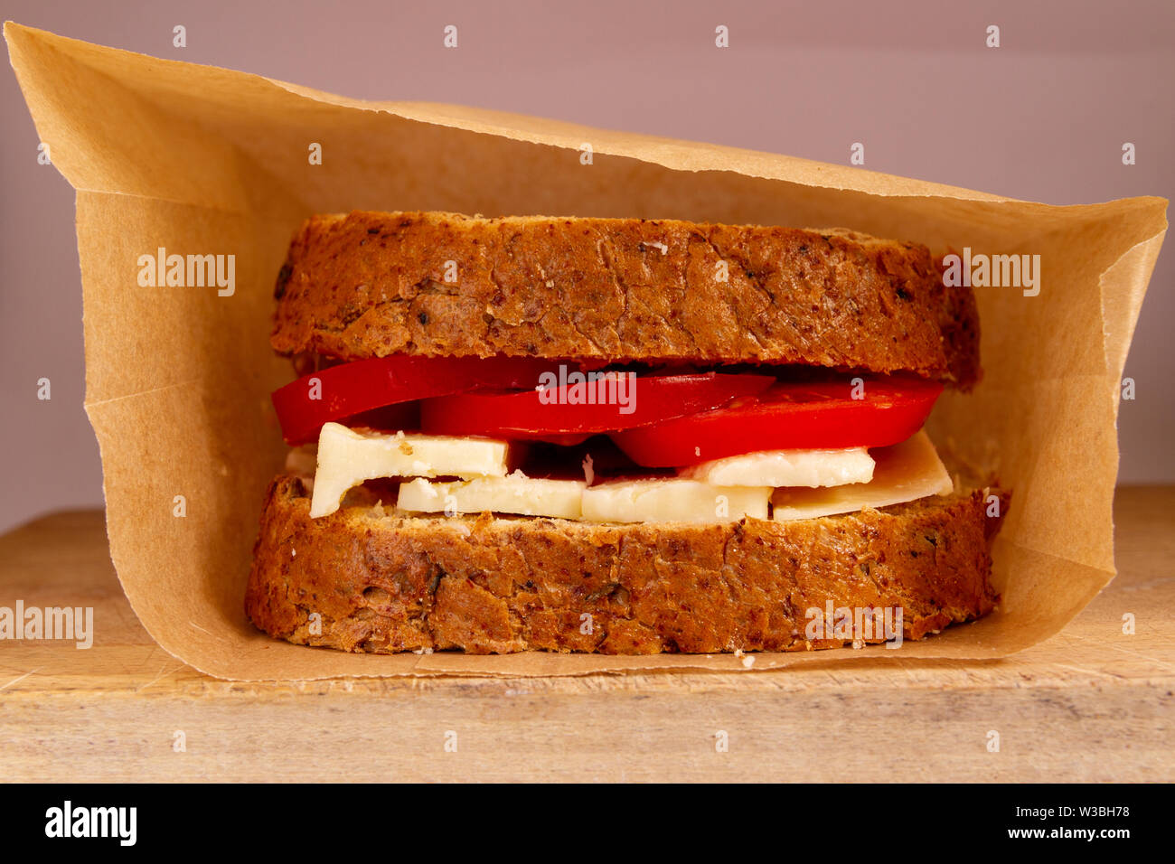Regarder directement dans un sac brun reposant sur une planche à découper en bois, montrant un fromage et tomate sandwich sur granary Banque D'Images